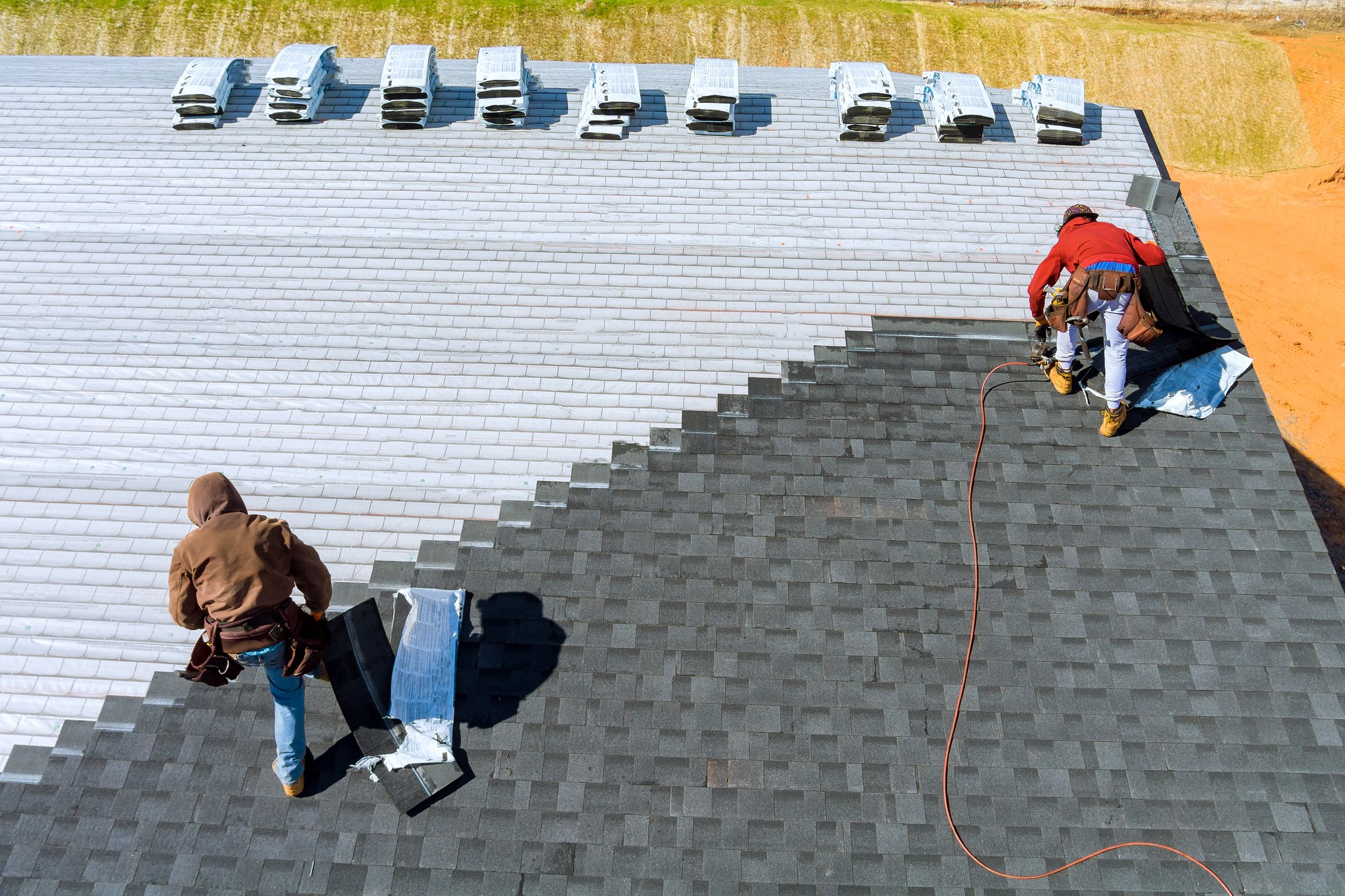 Worker hands installing bitumen roof shingles with air hammer and nailgun